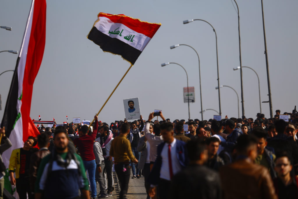 علم عراقي يرفرف في مظاهرة وسط حشد من الطلاب، وأحد الطلاب يلتقط صورة للعلم من الأسفل.